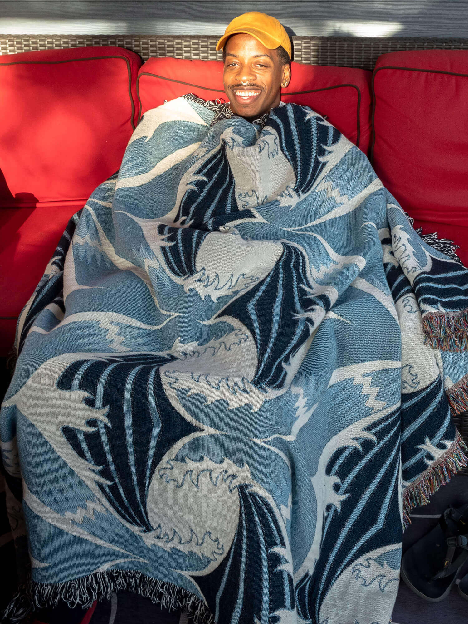 Phillip outside on red couch wearing wave love ocean and sky blue blanket