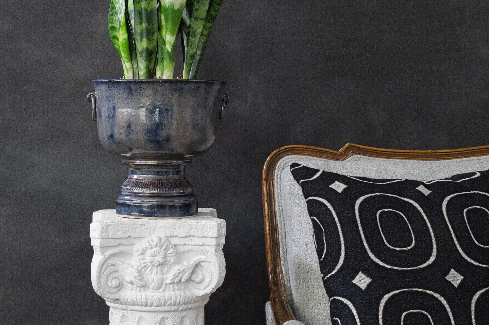 ceramic pot and pillow in a staged setting with an antique grey and brown wood couch and a white podium